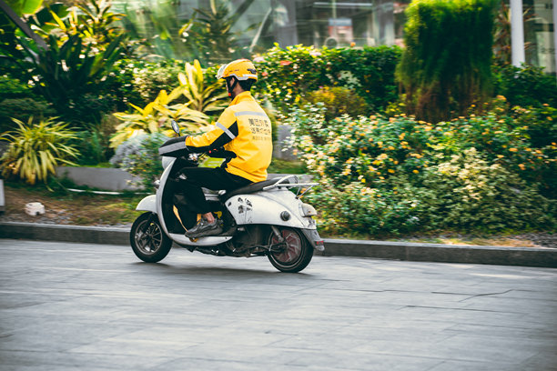 一名穿着黄色制服的快递员骑着电动车穿行在中国的城市街道上。图片下载