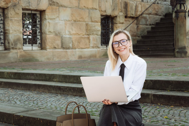 穿着商务服装的年轻女性在街上使用笔记本电脑。学习，工作。高质量照片图片下载