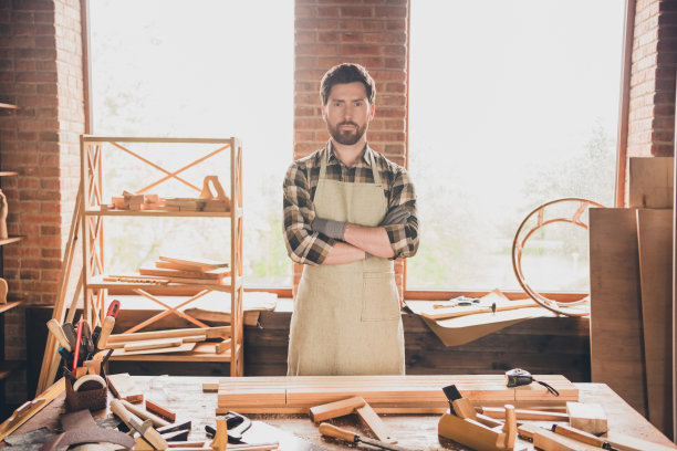 自信的男人穿着格子衬衫和围裙，双手交叉，站在车库里准备开始木工制作的肖像照片图片下载