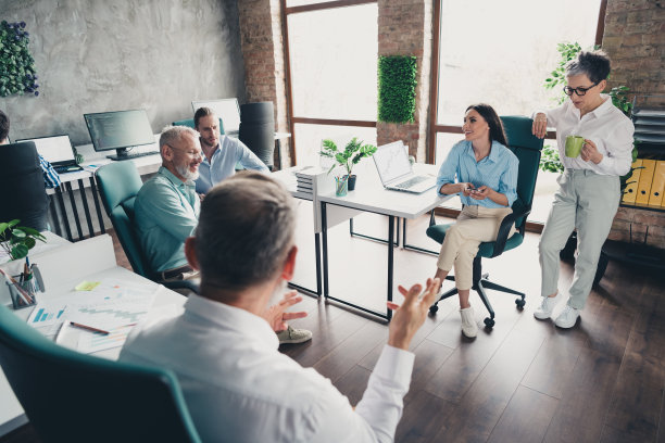 全景照片，展示了在明亮的办公室中，团队成员围成一圈讨论工作，进行成功的会议。图片下载