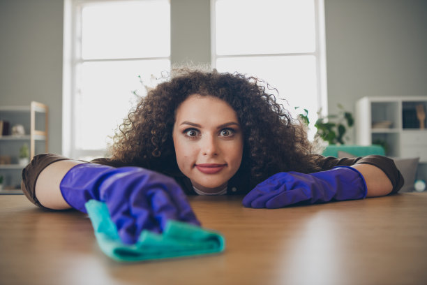 特写照片：快乐的年轻家庭主妇独自在舒适的阁楼公寓中用抹布清洁木质桌面。图片下载