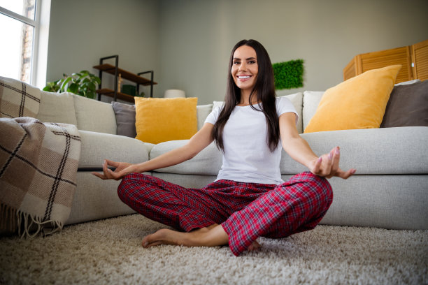全身照片，漂亮的年轻女士坐在地板上冥想，穿着睡衣，周末现代室内公寓内。图片下载