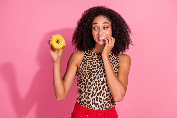 可爱的年轻女士在粉色背景下穿着时尚的豹纹服装，面露压力，手里拿着甜甜圈的肖像照片图片下载