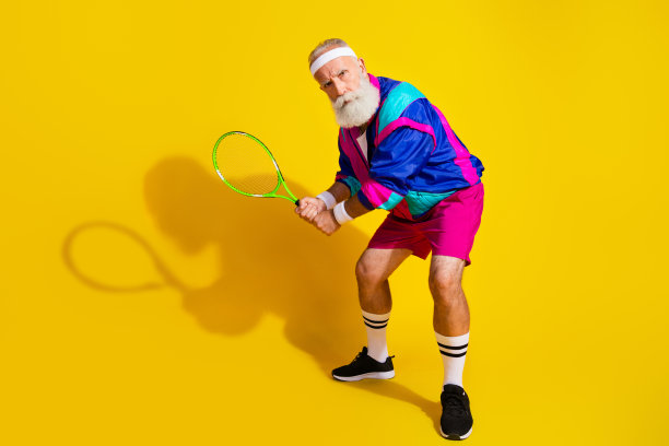 全身照片横幅，搞笑的老年运动员认真打网球，穿着时尚复古运动服，背景为黄色。图片下载