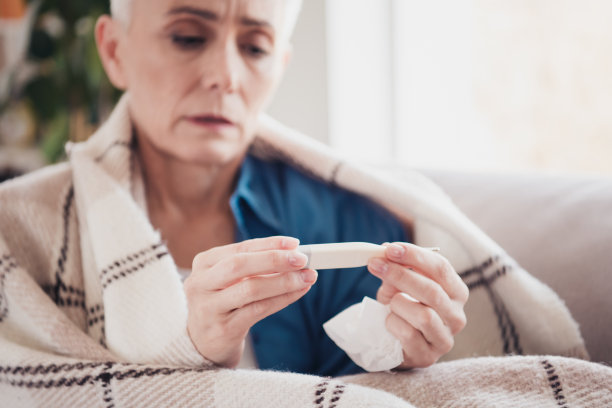 一位和蔼的老年女士在明亮的公寓室内穿着蓝色衬衫，手持温度计的特写照片图片下载