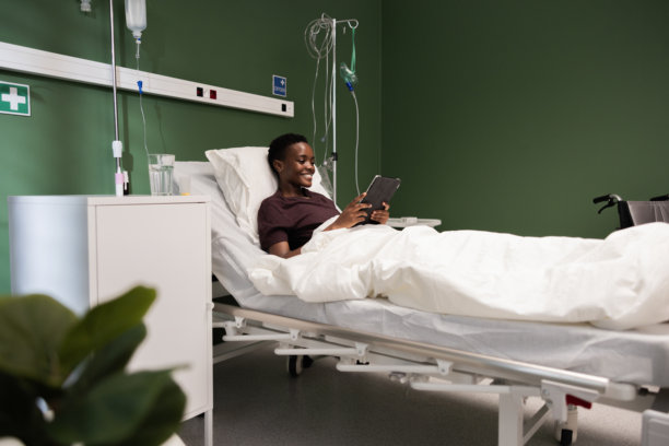 非洲女性躺在医院床上，翻阅平板电脑上的照片，回忆快乐的时光。图片下载