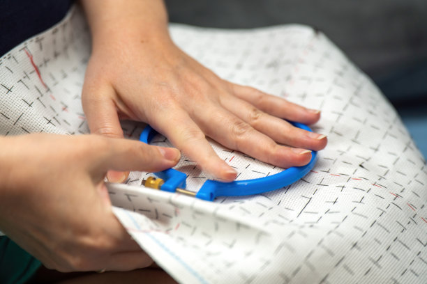 特写照片捕捉到一对女性的手巧妙地将标记好的布料插入刺绣圈中。细腻的动作反映了纺织艺术中的创造力、传统和对细节的关注。图片下载