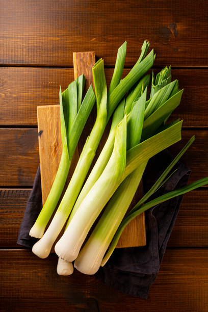 一束新鲜的韭菜放在木质背景上，垂直照片俯视图图片下载
