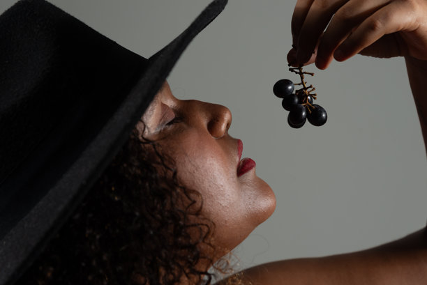 美丽的黑人女性特写肖像，戴着帽子，手里拿着一串葡萄。摄影棚照片。图片下载