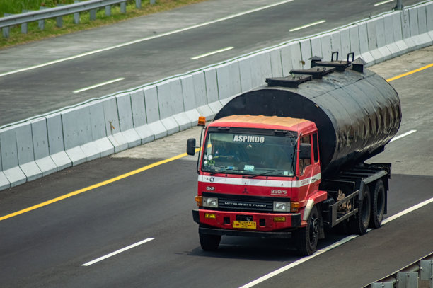 一辆红色三菱扶桑沥青运输车在印尼的收费公路上，拍摄于2024年10月31日。这张照片适合用于交通、基础设施或物流相关的文章。图片下载