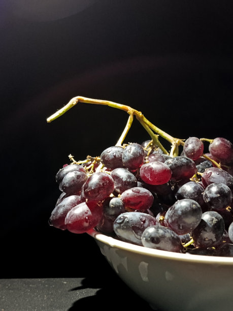 一串黑葡萄放在白色杯子里，背景为黑色。水滴上的无核葡萄在黑色背景下的枝条上。黑暗的食物照片。黑色无核葡萄。文本背景。图片下载