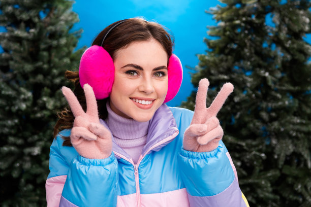 特写照片，阳光明媚的寒冷日子里，穿着舒适外套的可爱女士在森林中散步，面带微笑，做出胜利手势。图片下载