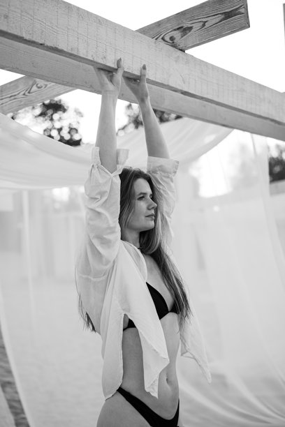 一位迷人的长发女孩在水边的沙滩上散步的肖像。穿着泳衣和衬衫的年轻女性在河边迎接夏日的黎明。黑白照片。图片下载