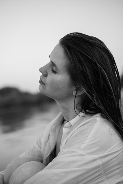 一位迷人的长发女孩在水边的沙滩上漫步的肖像。穿着泳衣和衬衫的年轻女性在河边迎接夏日的黎明。黑白照片。图片下载