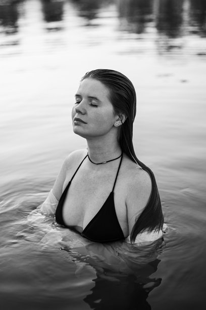 一位迷人的长发女孩在水边的沙滩上漫步的肖像。穿着泳衣和衬衫的年轻女性在河边迎接夏日的黎明。黑白照片。图片下载