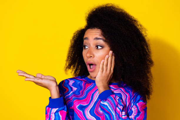 漂亮年轻女孩的照片肖像，穿着时尚多彩的蓝色服装，手持空白空间，表情害怕，背景为黄色。图片下载