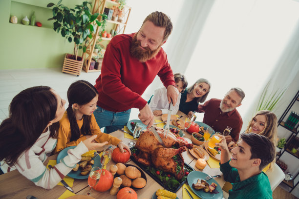一家人一起庆祝感恩节的照片，男人在室内切割传统主菜烤火鸡。图片下载