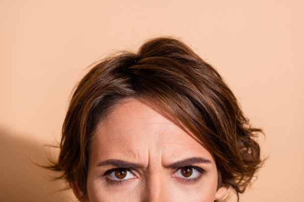 裁剪的照片肖像，漂亮年轻女士愤怒地看着，遮住脸部，背景为米色。图片下载