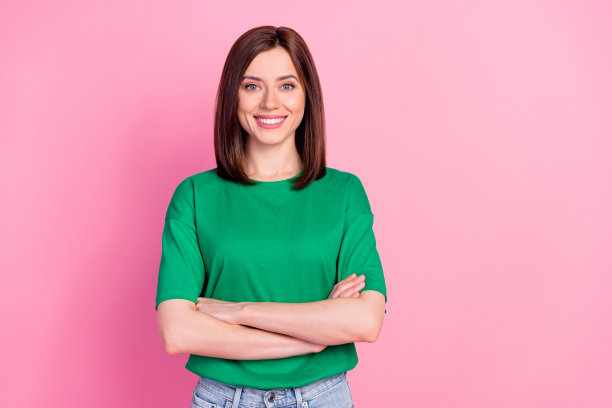 迷人年轻女性创业公司首席执行官的照片肖像，双臂交叉，露出灿烂的微笑，穿着时尚的绿色服装，背景为粉色。图片下载