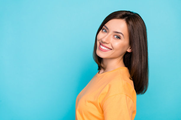 特写侧面照片，快乐可爱的女士穿着时尚的橙色衣服，享受着理发，背景为蓝色。图片下载