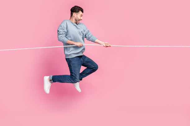 决心满满的男士侧面照片，跳起拉动绳子，享受惊人的折扣，背景为柔和色彩。图片下载