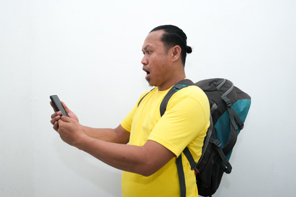 一位亚洲男子手持手机，面露震惊表情的照片图片下载