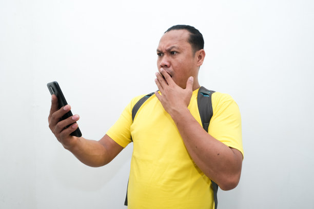 一位亚洲男子手持手机，面露震惊表情的照片图片下载