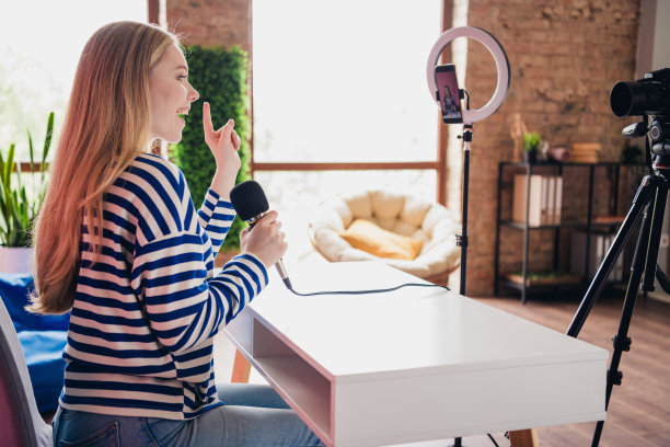 室内快乐女孩博主侧面照片，正在用麦克风进行采访直播。图片下载