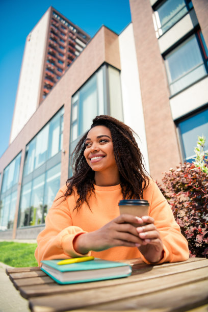 穿着橙色毛衣的漂亮快乐女士在城市街道上户外喝早晨饮品的竖版照片图片下载