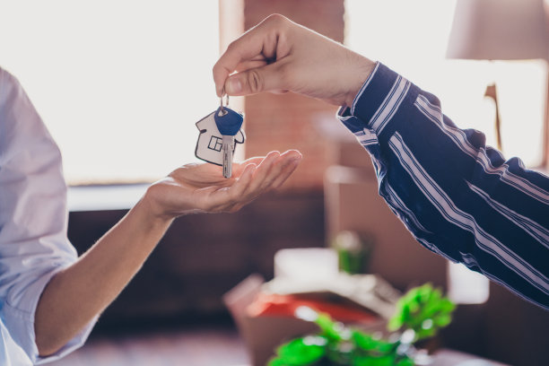 裁剪的照片显示人们的手握着房屋钥匙，穿着衬衫和牛仔裤，准备搬入新家，温馨的日光照耀着室内客厅。图片下载
