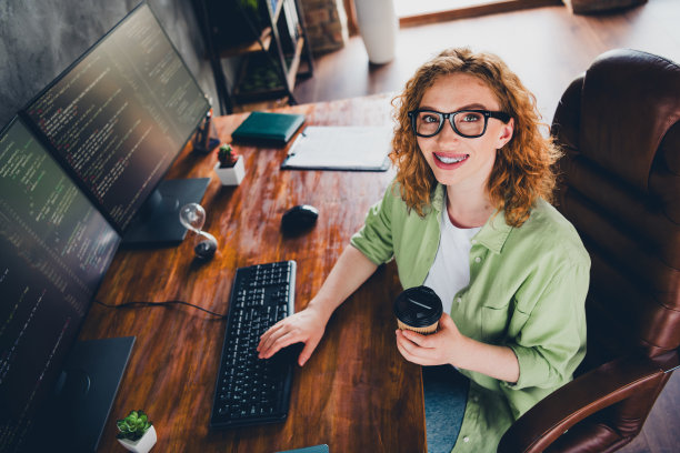 俯视照片中，一位可爱积极的女经纪人穿着衬衫，戴着眼镜，正在室内工作场所的现代设备上打字，享受饮品。图片下载