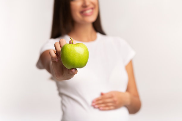怀孕女孩在白色背景下展示触碰肚子的药丸，裁剪过的图片图片下载