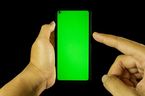 亚洲男子的手握着一部黑色背景下带有空白绿色屏幕的安卓智能手机图片下载