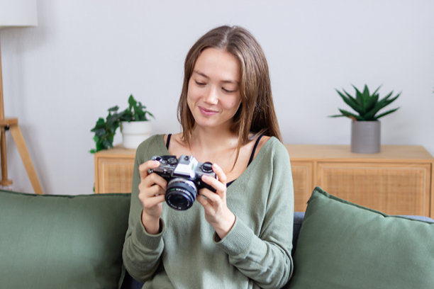 年轻女性在家中微笑着拿着一台复古相机，查看照片。图片下载