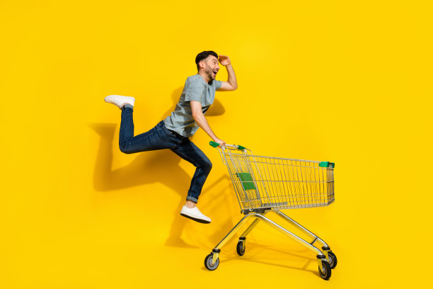 兴奋无忧的人在黄色背景下跳跃，手中拿着空购物车的全身侧面照片图片下载
