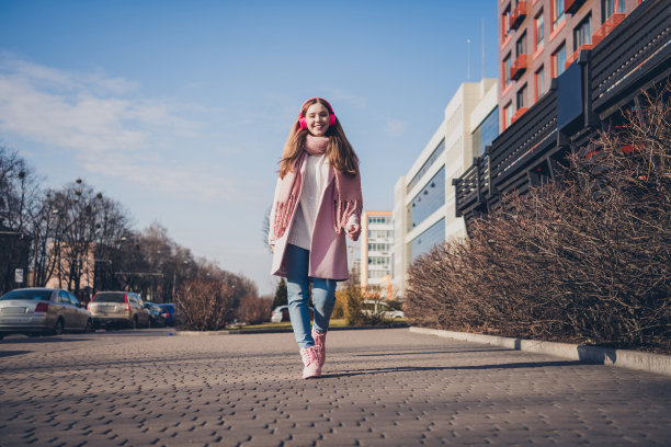 年轻女孩穿着外套在城市中心街道上走路，听着音乐的全身照片图片下载