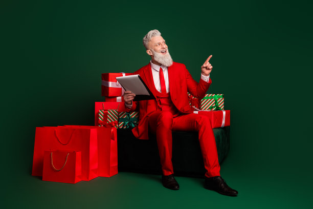 现代时尚圣诞老人礼物愿望清单的全身照片，手指指向绿色背景上的空白区域，适合圣诞节使用。图片下载
