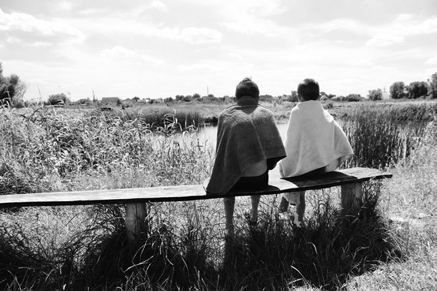 两个孩子在河边的长椅上晒太阳，游泳后用毛巾裹着。黑白照片，男孩们在夏季假期时在水边休息。图片下载