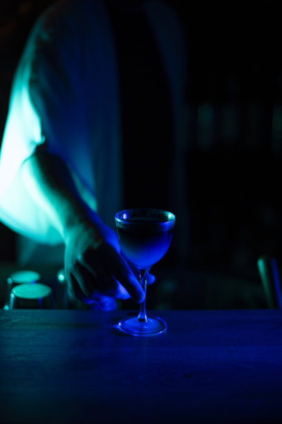调酒师在蓝色低调灯光下将一杯双层鸡尾酒递给顾客，竖版图片图片下载