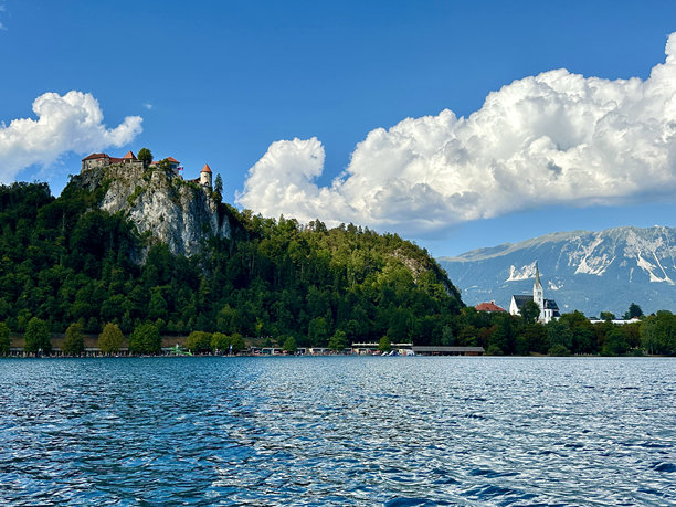 这张照片捕捉到了一艘船在湖上，背景是斯洛文尼亚夏日壮丽的山脉风景。图片下载
