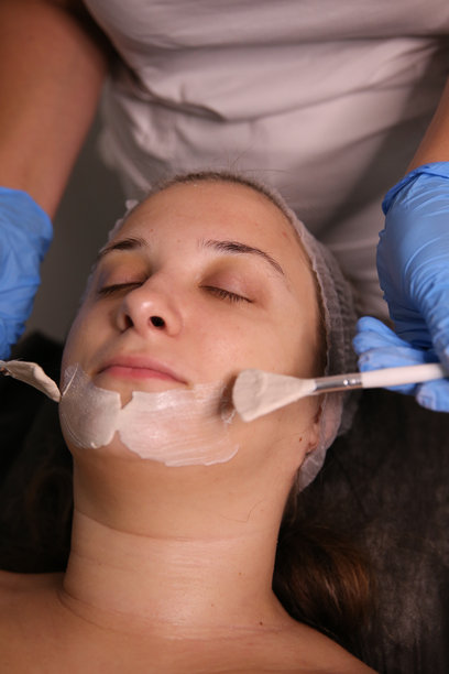 一位专业美容师在患者脸上涂抹滋养霜。保湿、清洁和面部护肤。美容程序的库存照片图片下载