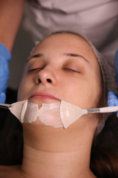 一位专业美容师在患者脸上涂抹滋养霜。保湿、清洁和面部护肤。美容程序的库存照片图片下载