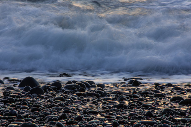 在太平洋西北地区，日落时拍摄的长时间曝光照片，展现了海浪涌向黑色卵石海滩的景象。图片下载