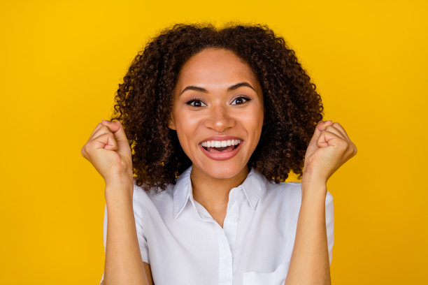 特写照片，快乐的女孩为体育团队冠军加油，拥有漂亮的波浪形发型和灿烂的笑容，背景为黄色。图片下载