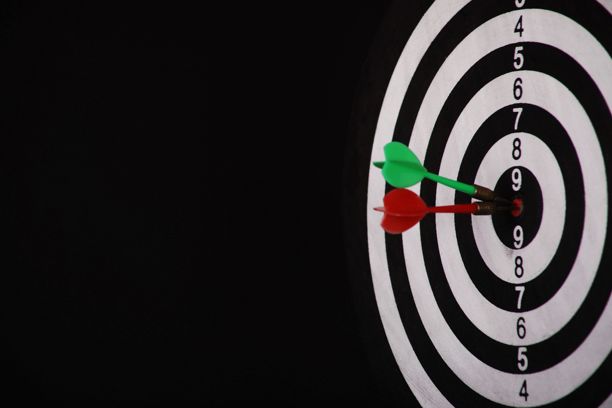 黑色背景下，红色和绿色飞镖近乎命中靶心的飞镖盘特写。图片下载