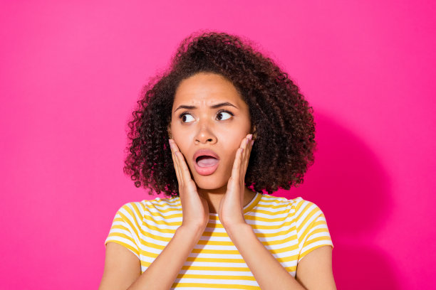 特写照片：年轻迷人的女孩用手触摸脸颊，张嘴露出震惊和兴奋的表情，背景为粉色，显得孤立而危险。图片下载