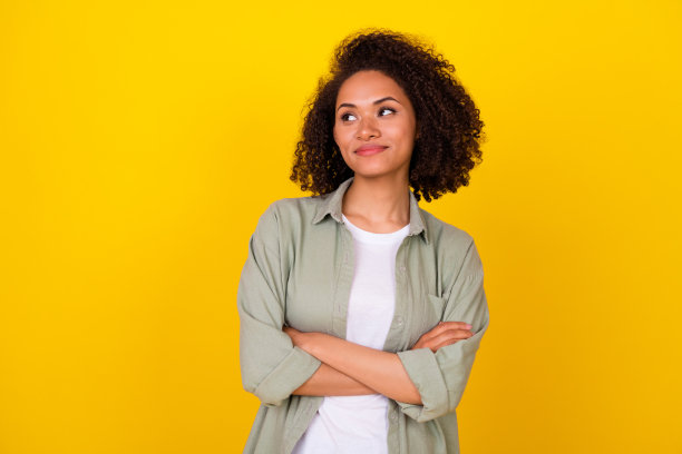 年轻女士的照片肖像，卷发，思考完美的商业策略，穿着时尚的卡其色服装，背景为黄色。图片下载