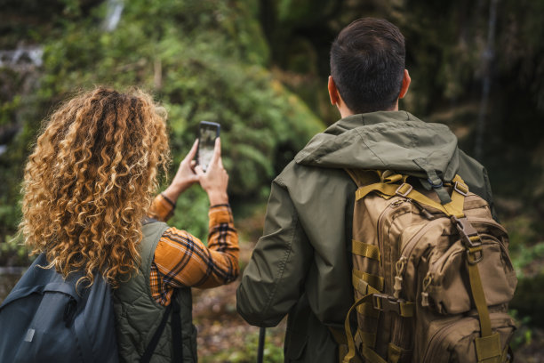 背影的登山夫妇，丈夫和妻子在拍摄瀑布的照片图片下载
