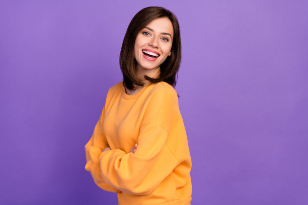 穿着橙色秋季时尚服装的可爱美女侧面照片，展现灿烂的微笑，背景为紫色。图片下载