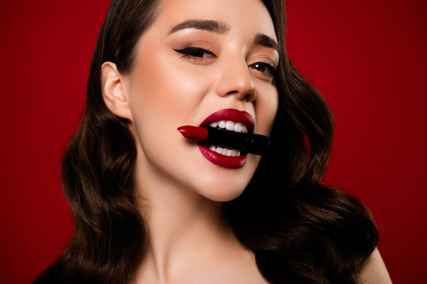 特写照片，迷人的模特在红色背景下涂抹化妆膏。图片下载